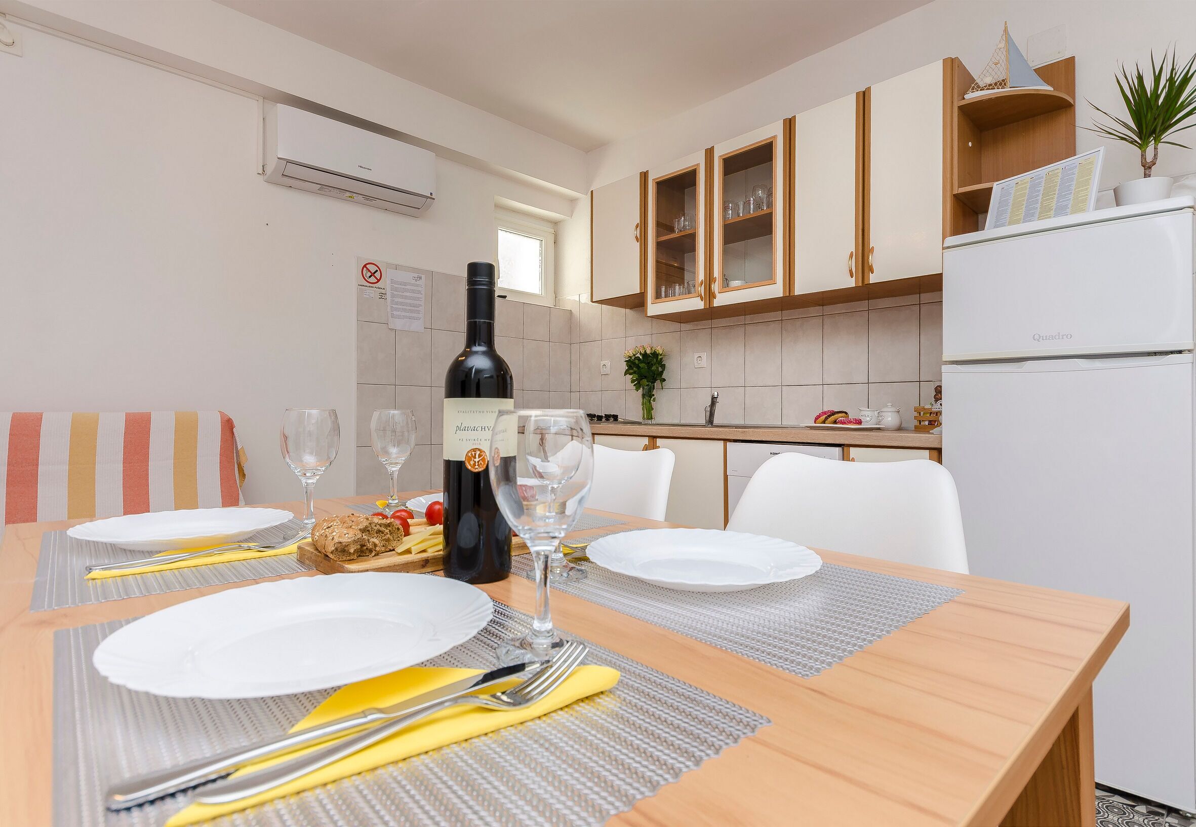 A dining area with a wooden table set for two, a bottle of wine, and a menu on the wall.