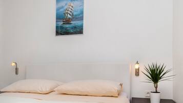 A bedroom with a bed, a nightstand with a plant, and a painting on the wall.