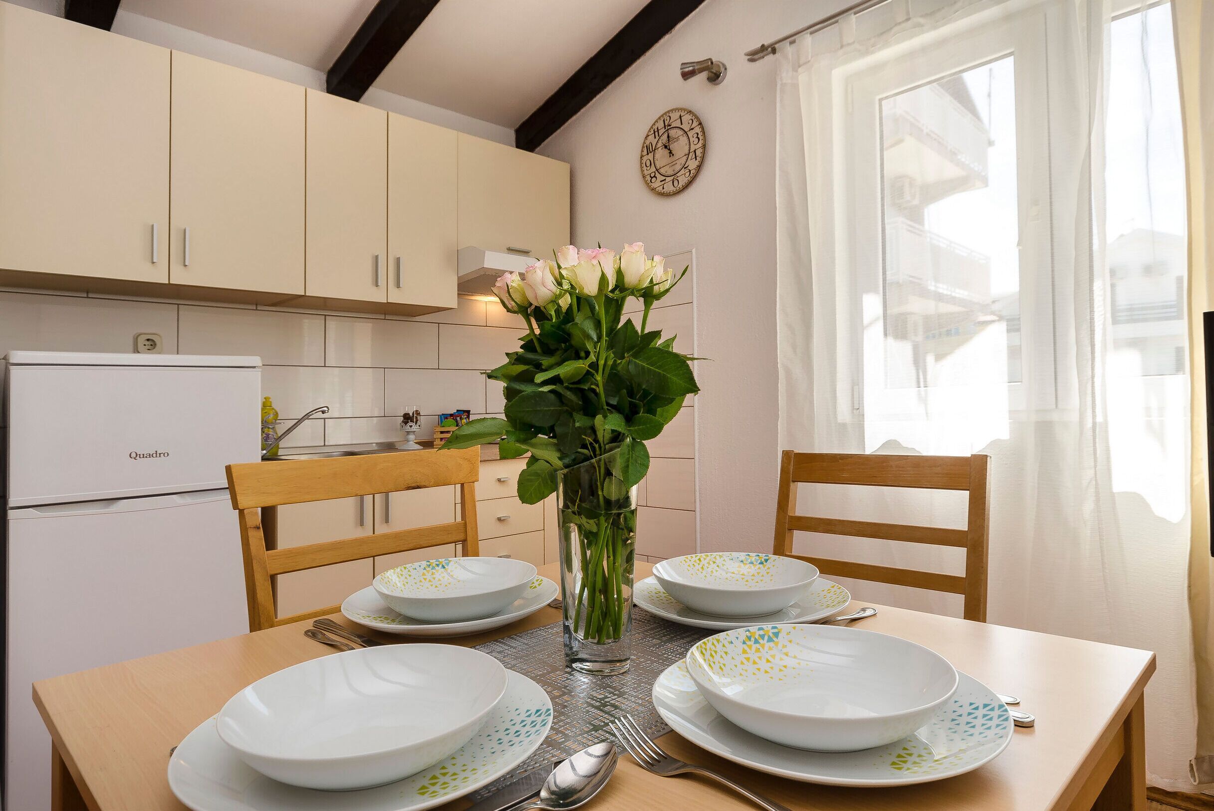 A dining table set with plates, a vase with flowers, and a clock on the wall.