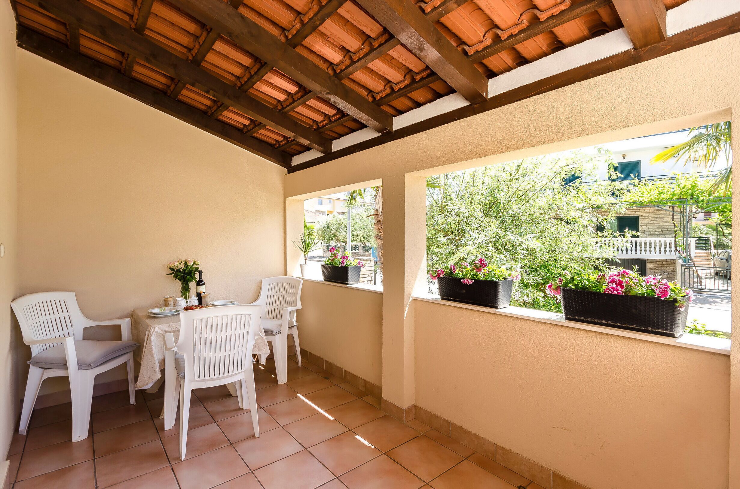 A covered patio with a table and chairs, potted plants, and a view of the street.