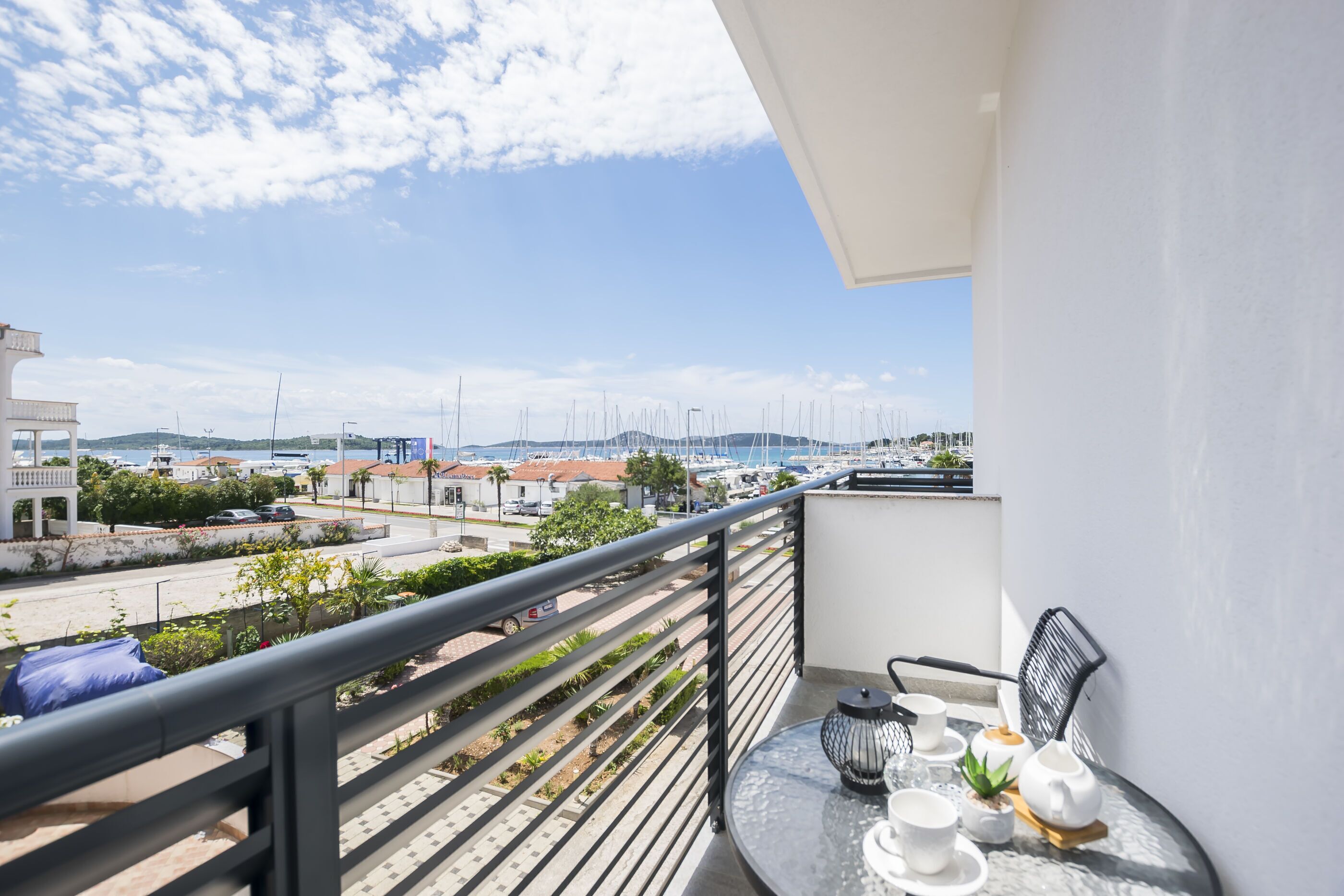 A balcony with a table set for tea, overlooking a marina with boats and buildings.