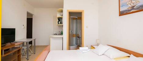Une chambre d’hôtel avec un lit, un bureau, une télévision, une douche et un tableau au mur.