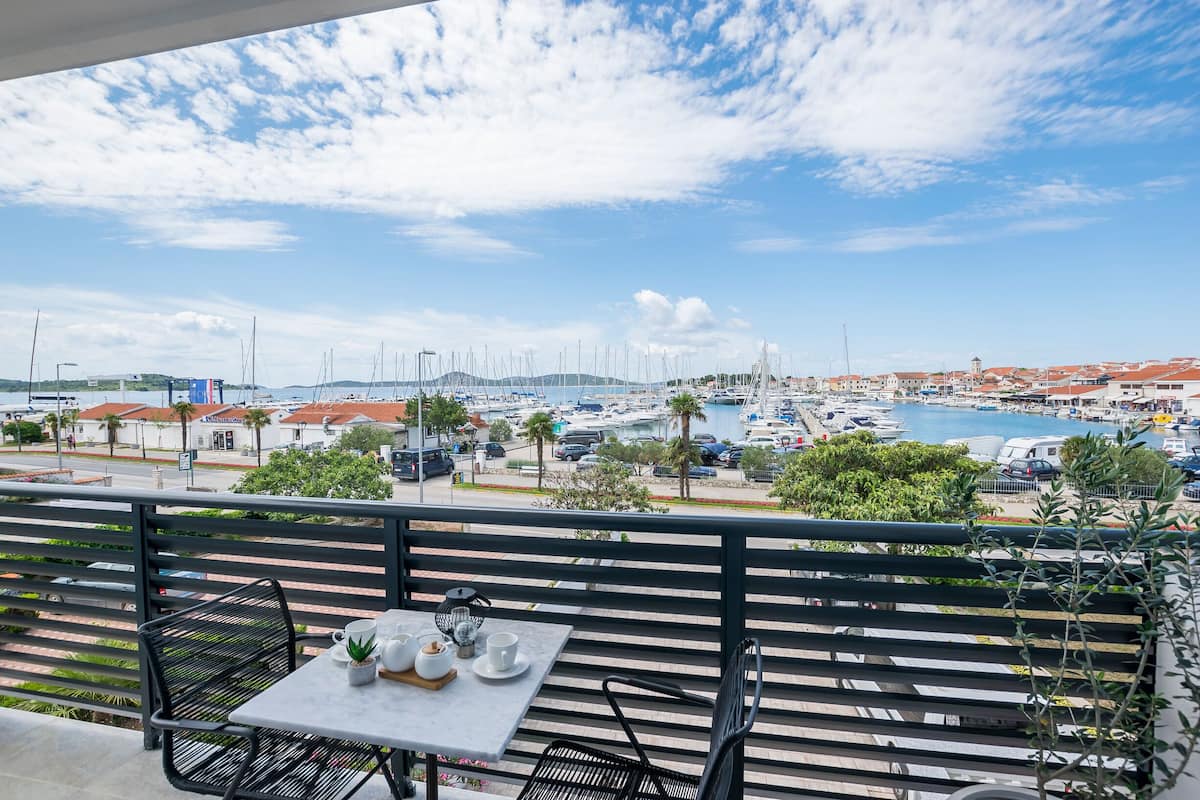 Varanda com mesa e cadeiras com vista para um porto cheio de barcos e edifícios.