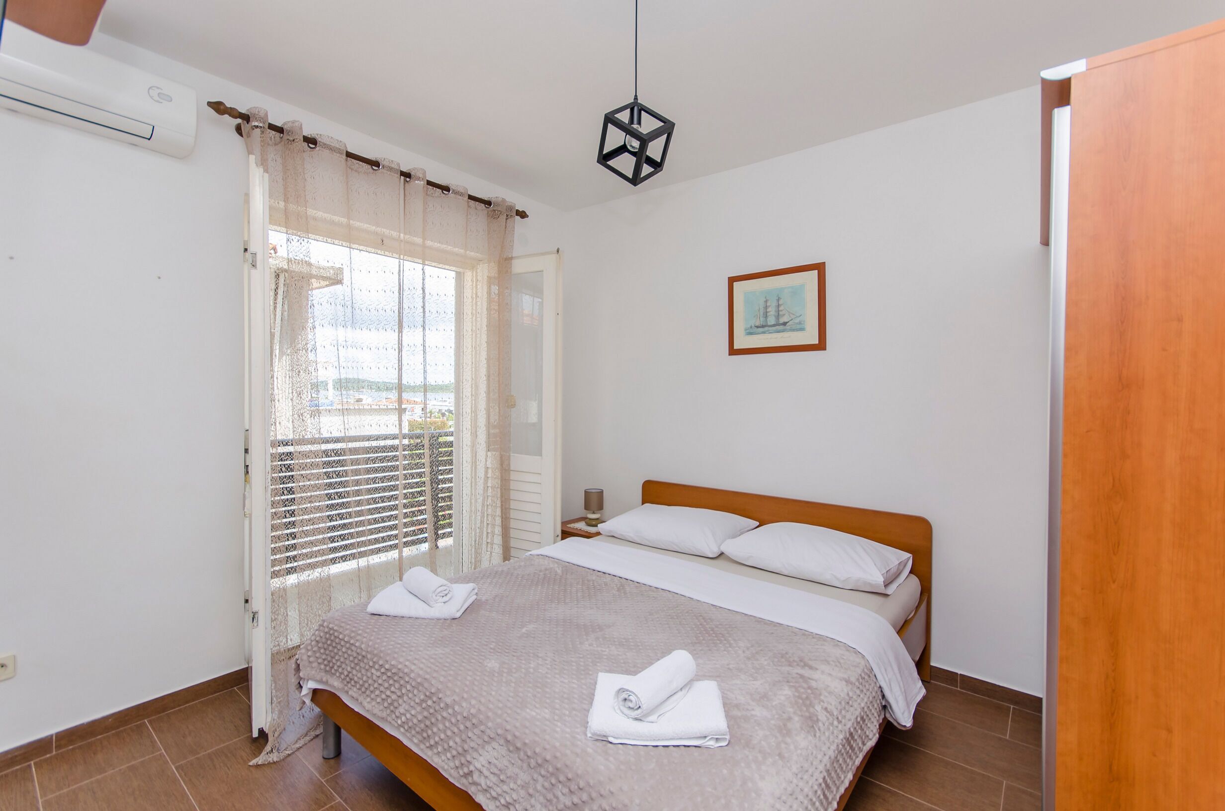 A bedroom with a bed, a window with curtains, a bedside table, and a hanging light fixture.