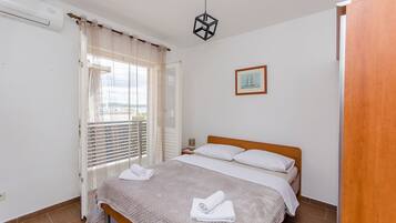 Un dormitorio con cama, ventana con cortinas, mesita de noche y lámpara colgante.