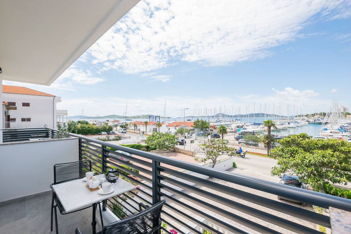 Varanda com mesa posta para chá, com vista para uma marina com barcos e céu claro.