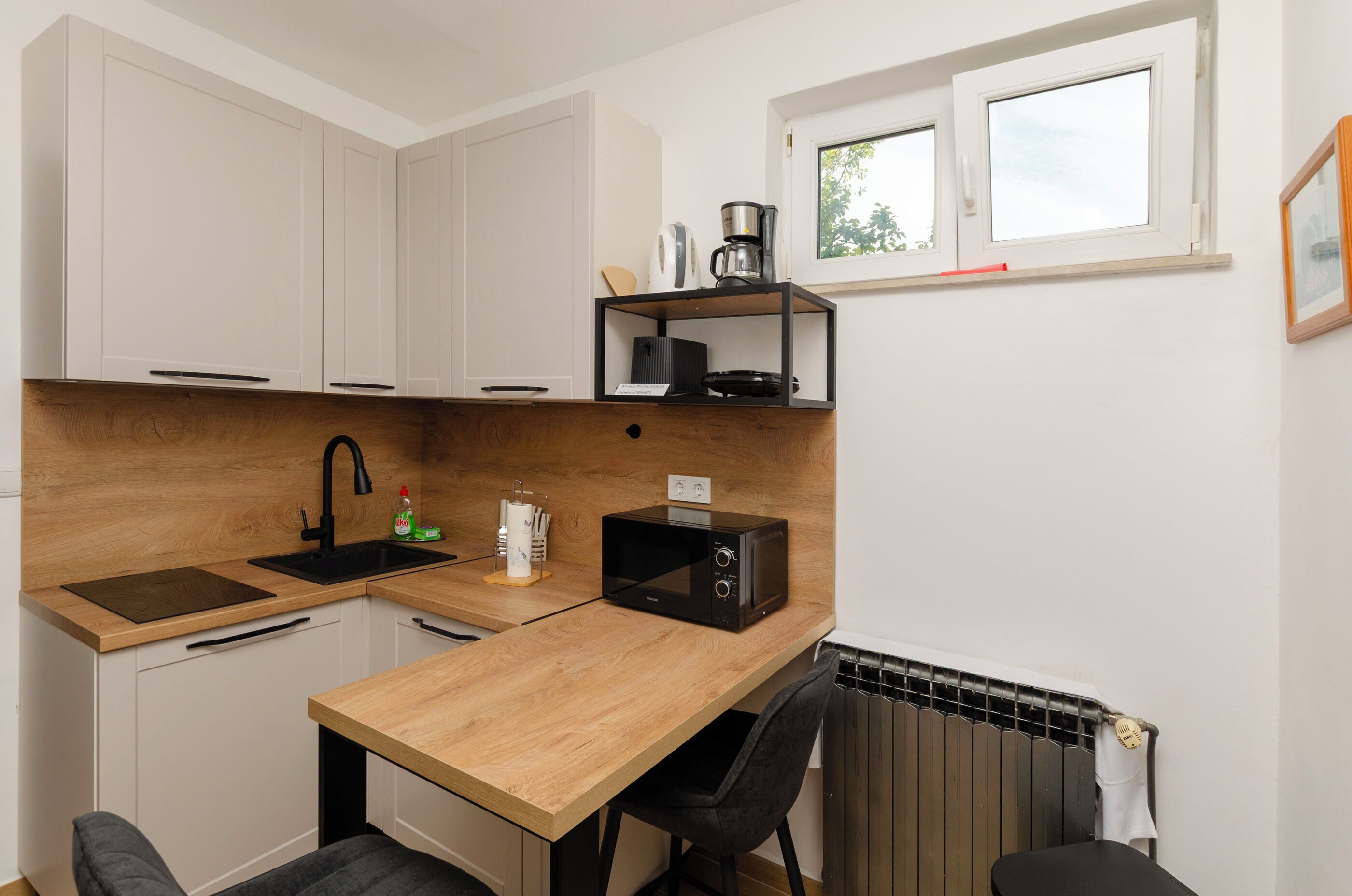 A compact kitchen with a wooden countertop, a black microwave, a coffee maker, and a window above the sink.