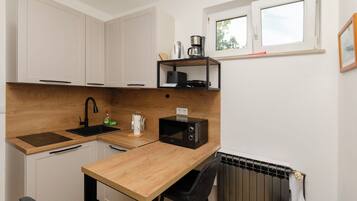 Cocina compacta con encimera de madera, microondas negro, cafetera y ventana sobre el fregadero.