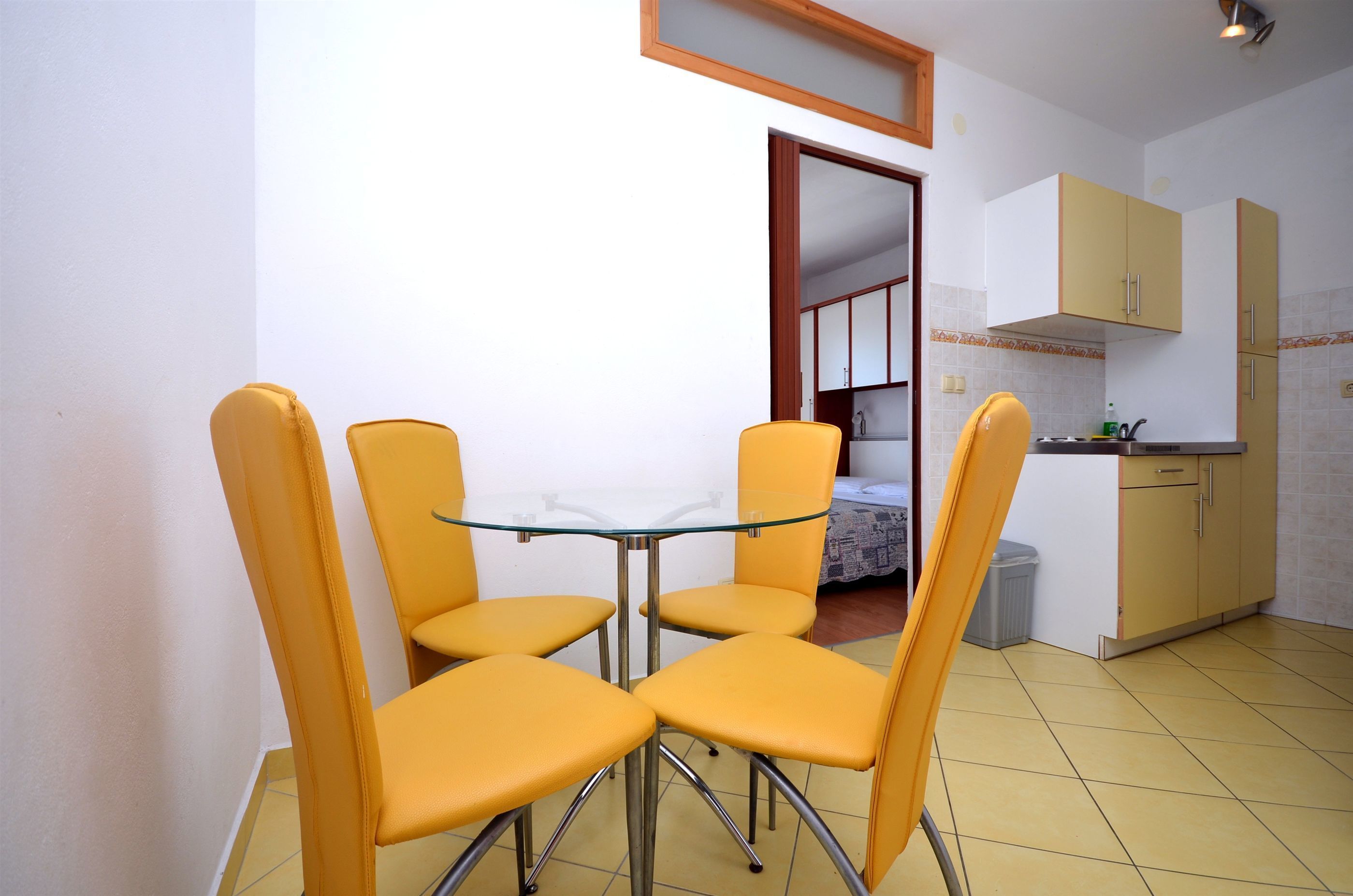 Una cucina compatta con mobili gialli, un tavolo in vetro e quattro sedie gialle.