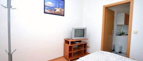 A bedroom with a bed, a television on a wooden stand, a coat rack, and a picture on the wall.