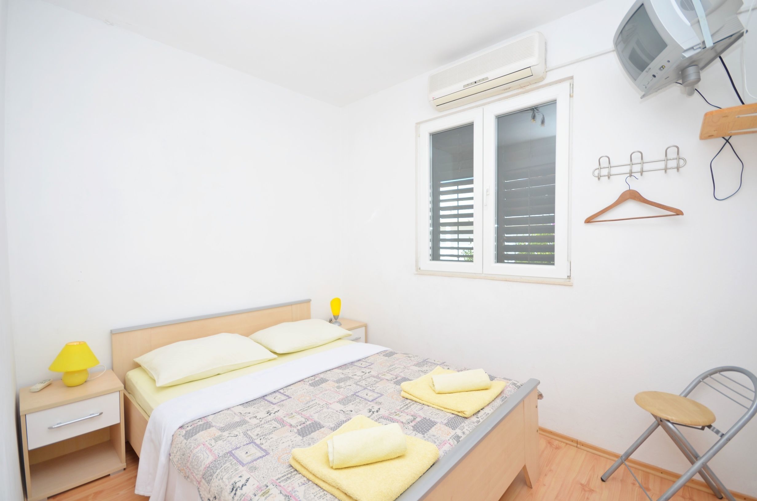 A bedroom with a bed, bedside table, lamp, and a window with blinds.