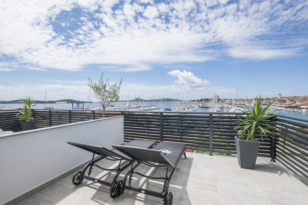 Terraço no telhado com mesa e cadeiras, plantas em vasos e vista para uma marina com barcos.