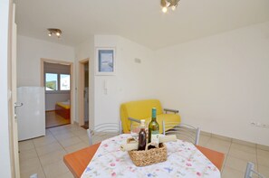 A dining area with a table set for two, featuring a floral tablecloth, a wicker basket, a bottle of wine, and a glass. - Apartments Marija (Hvar)