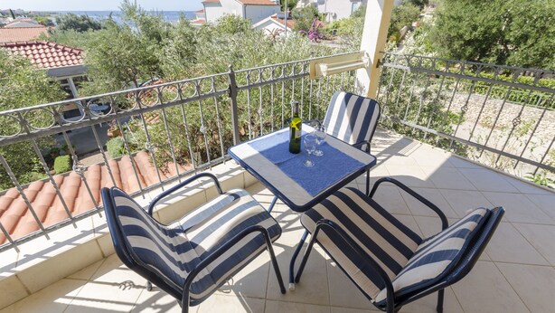 A balcony with a table and chairs, overlooking a coastal area with houses and vegetation. - Apartments Marija (Razanj)