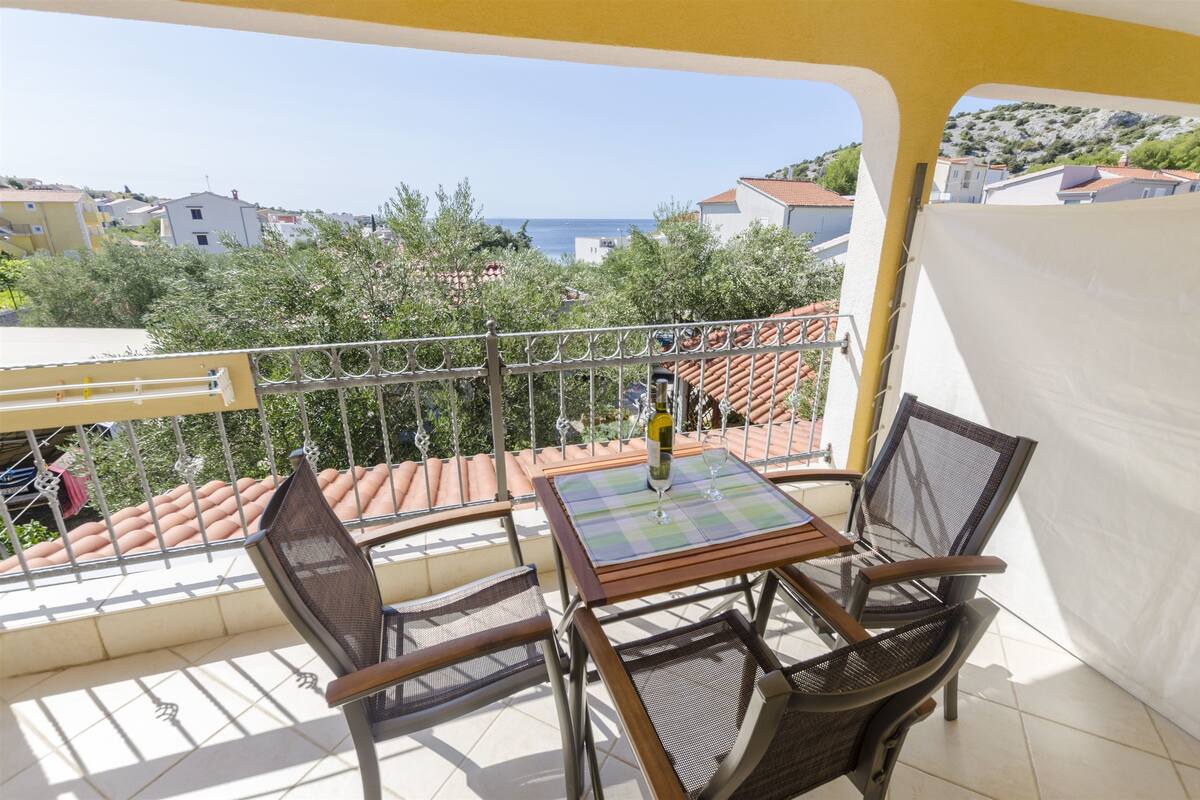 A balcony with a table and chairs, overlooking a coastal area with buildings and trees.