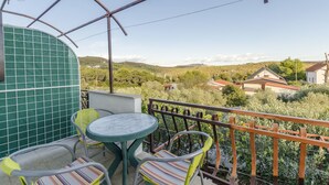 A balcony with a table and chairs, overlooking a rural landscape with houses and greenery. - Apartments Oliva (Maslinica)