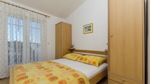 A bedroom with a bed, wooden wardrobe, and a window with curtains. - Apartments Oliva (Maslinica)