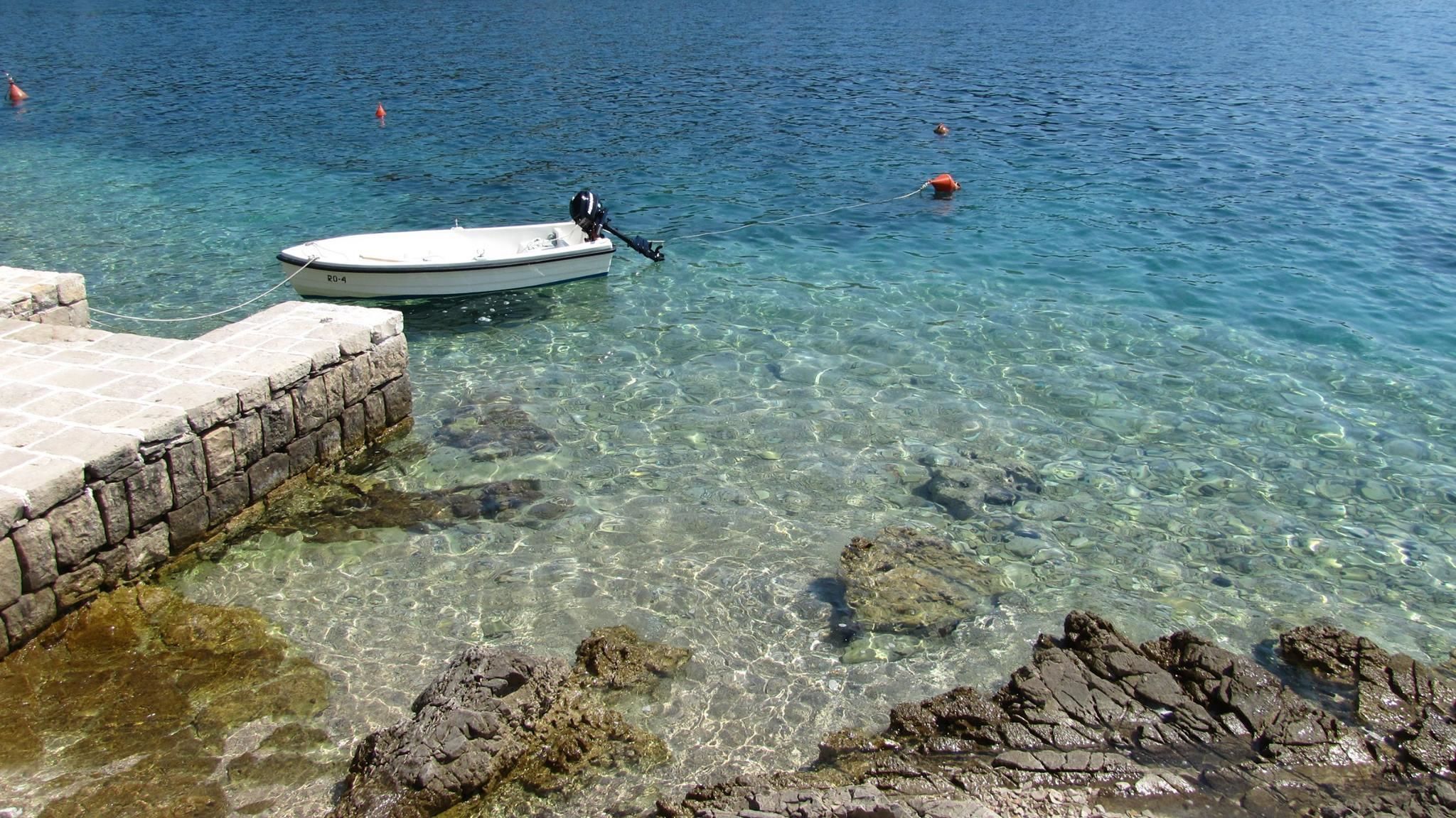 A boat docked at a rocky shore with clear water.
