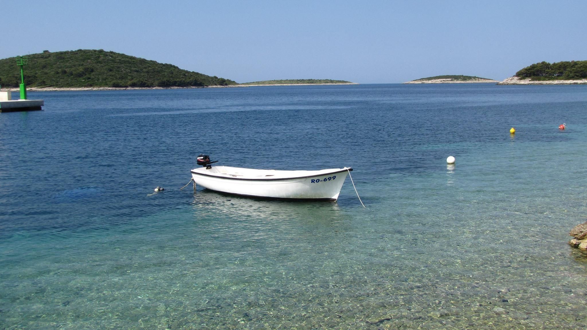 A small white boat with the registration number R0-699 anchored near a rocky shore with clear water.