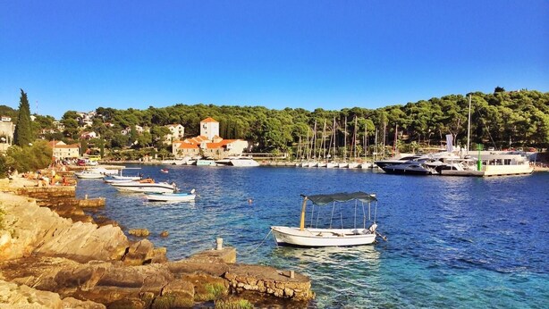 A coastal marina with boats docked, rocky shoreline, and buildings in the background. - Apartments Oliva (Maslinica)