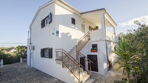 A two-story building with a stone-paved entrance, a staircase with metal railings, and a small balcony with potted plants. - Apartments Oliva (Maslinica)