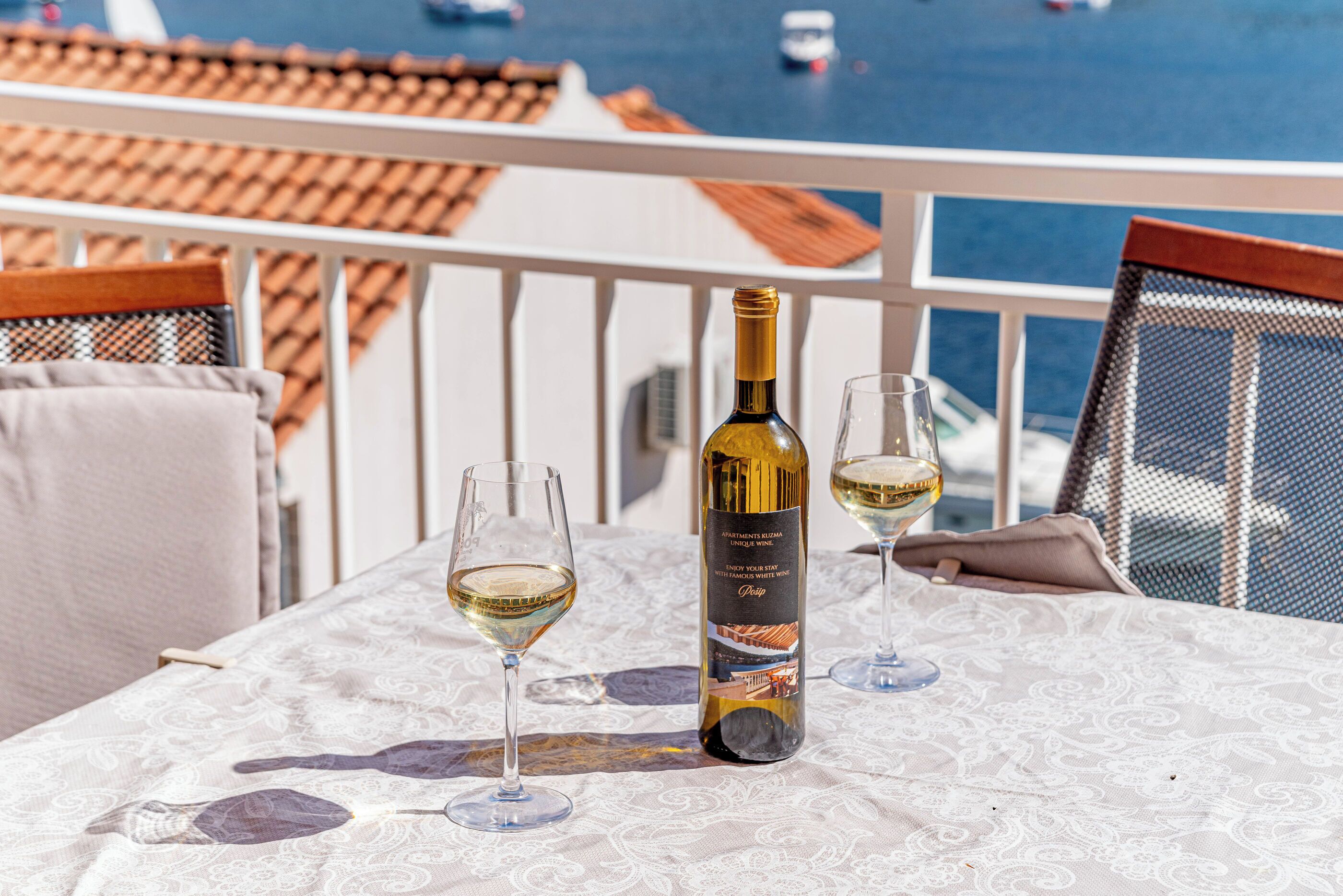 A table with a bottle of wine and two glasses on a balcony overlooking the sea.