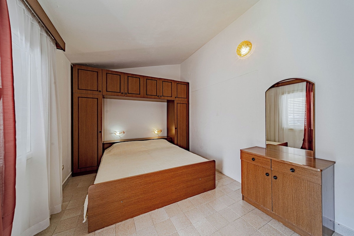 A bedroom with a wooden bed, a dresser, a mirror, and a wall-mounted light fixture.