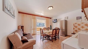 A compact living space with a sofa, dining table, chairs, a TV, a refrigerator, and a washing machine. - Apartments Vesna (Brna)