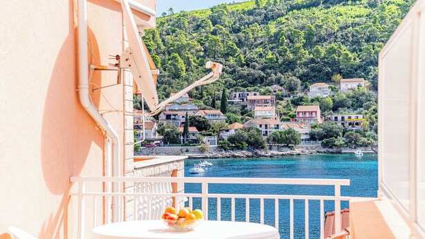 A balcony with a table and chairs, overlooking a coastal town with houses and a body of water. - Apartments Vesna (Brna)