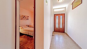 A hallway with a wooden floor leading to a room with a bed and a wooden door. - Apartments Vesna (Brna)