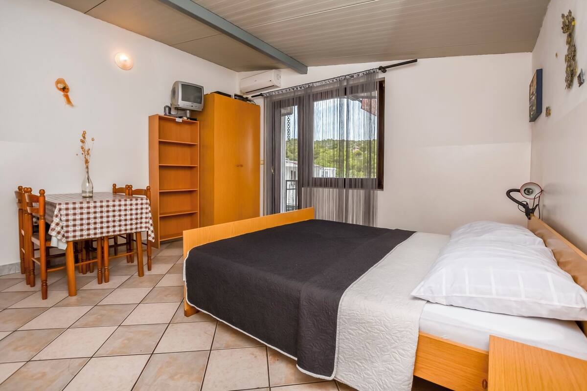 A bedroom with a bed, a table with chairs, a TV, and a window with curtains.