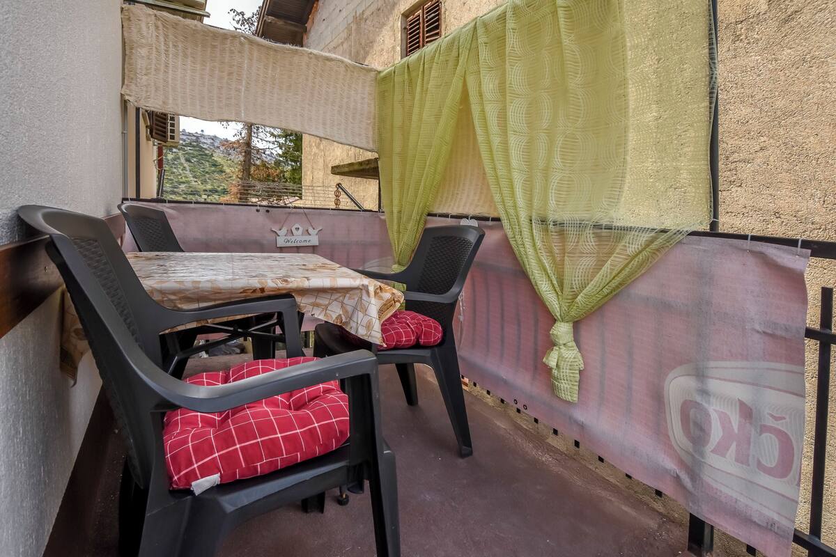 A balcony with a table and two chairs, a green curtain, and a sign reading "Welcome".