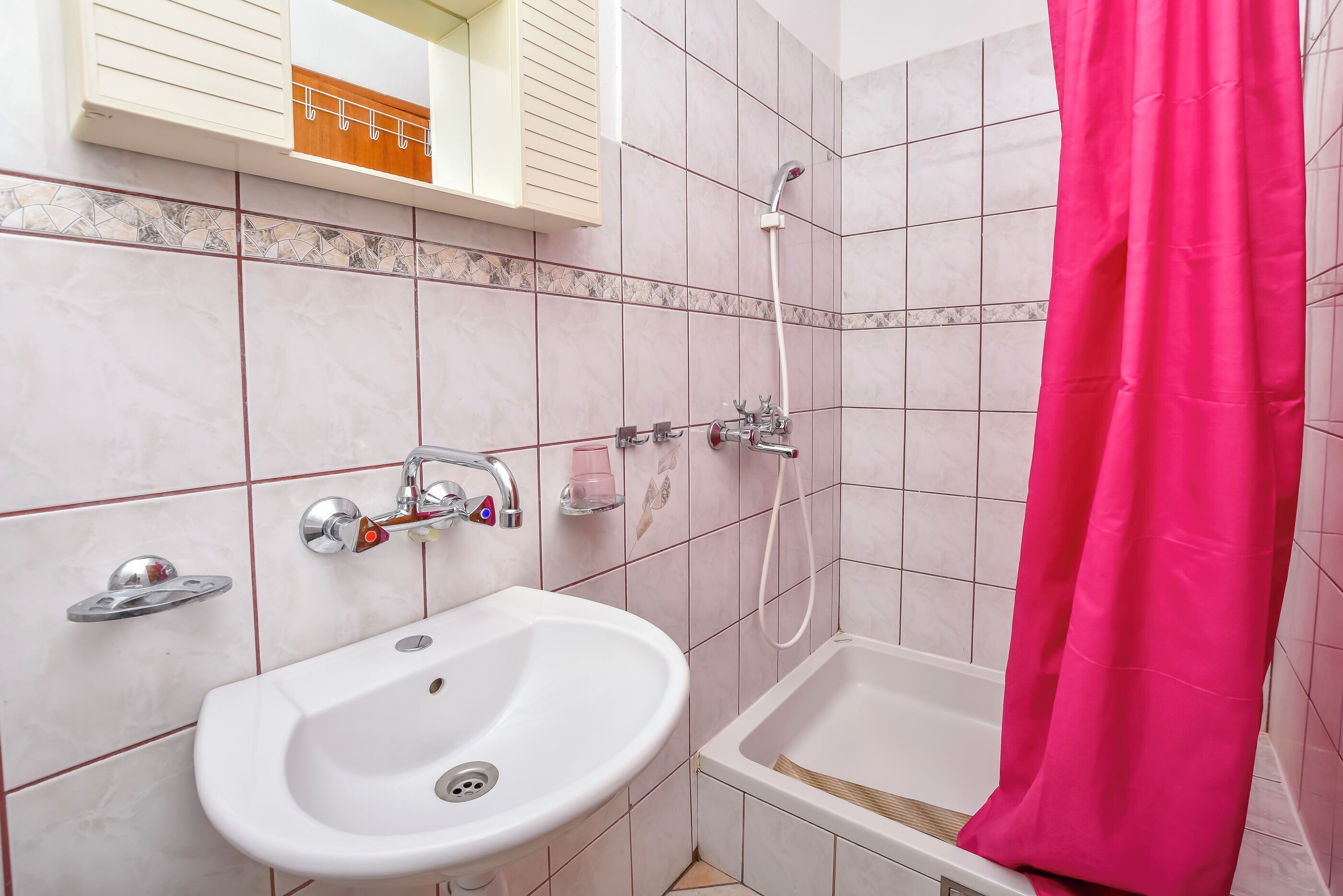 Ein Badezimmer mit einem weißen Waschbecken, einer Dusche mit rosa Vorhang und einem Spiegel mit Holzrahmen.