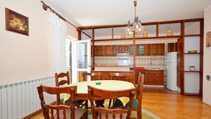 Ein Essbereich mit Holztisch und -stühlen, eine Küche mit Holzausstattung und einem Kühlschrank sowie eine Wandverkleidung mit Muster.