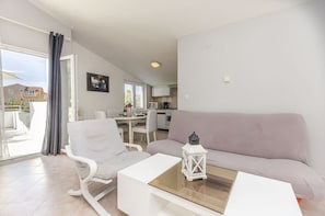 A modern living room with a sofa, a white armchair, a glass coffee table, and a kitchen in the background. - Apartments Manda (Vodice)