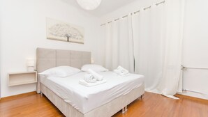 A neatly made bed with white linens and towels, a bedside table with a lamp, and a wall-mounted artwork of a tree.