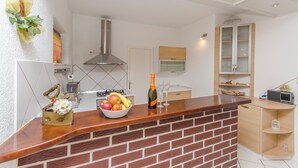 A modern kitchen with a brick backsplash, a wooden countertop, and a built-in stove. There is a fruit bowl with apples and bananas, a bottle of champagne, and a decorative plant on the counter.