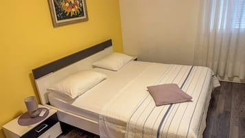 Ein Einzelzimmer mit Holzboden, einem Nachttisch mit Lampe und einem Gemälde an der Wand.