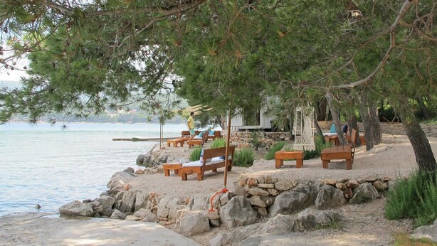 A beachside seating area with wooden benches and tables, a stone wall, and a view of the sea. - House Lara (Vrboska)