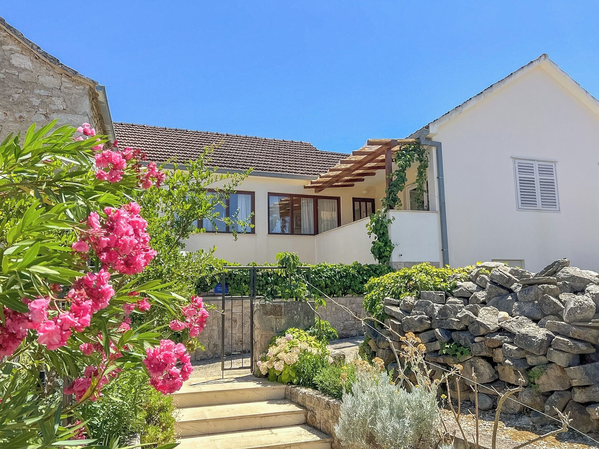 Un bâtiment blanc avec un toit en tuiles, un mur en pierre et un escalier en bois menant à un balcon.