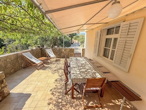 An outdoor patio with a table and chairs, a stone wall, and a view of the surrounding greenery.
