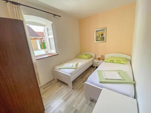 A small, well-lit bedroom with two beds, a window, and a painting on the wall. - House Lara (Vrboska)