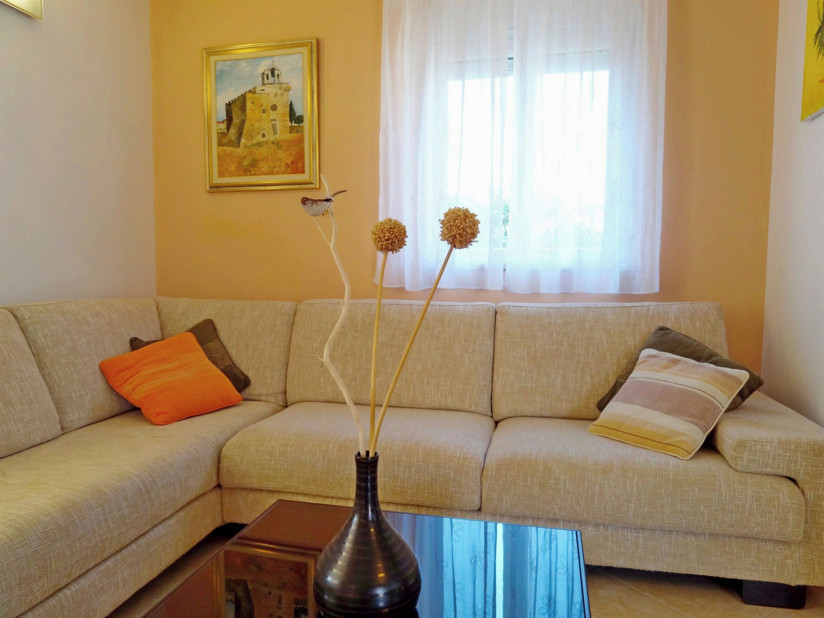 Ein Wohnzimmer mit einem beigefarbenen Sofa, einer Vase mit getrockneten Blumen und einem Bild an der Wand.