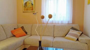 Ein Wohnzimmer mit einem beigefarbenen Sofa, einer Vase mit getrockneten Blumen und einem Bild an der Wand.