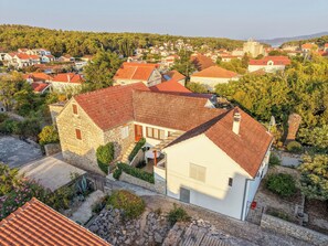 A stone house with a red-tiled roof, surrounded by other houses, set in a hilly area with trees. - House Lara (Vrboska)