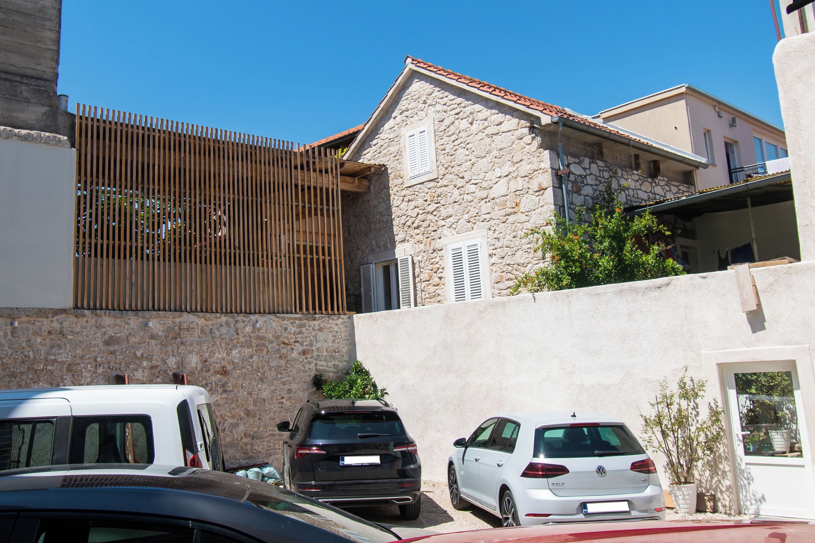 Una fila de coches aparcados frente a un edificio de piedra con techo inclinado y valla de madera.