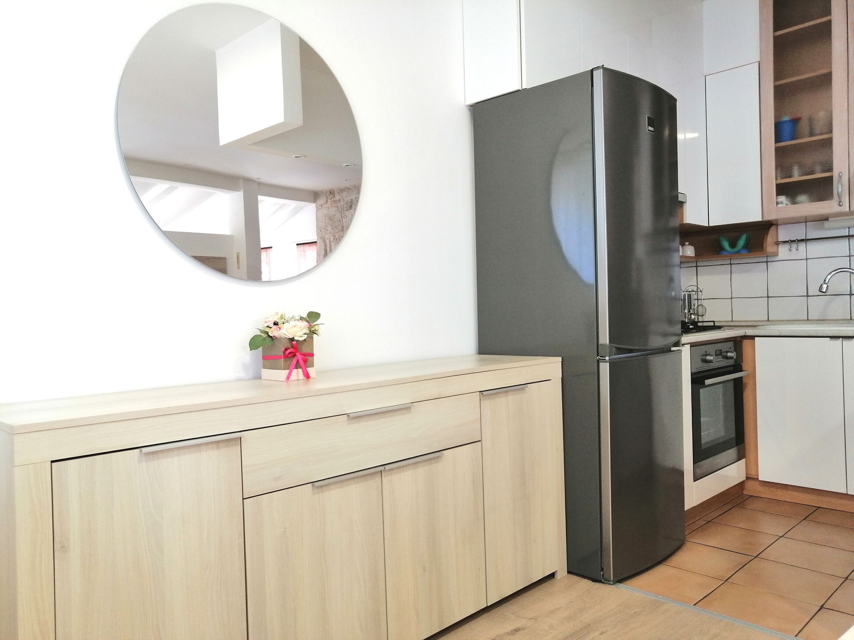 Eine Küche mit einem Edelstahlkühlschrank, einer Holz Arbeitsplatte, einem Spiegel und einer kleinen Pflanze.