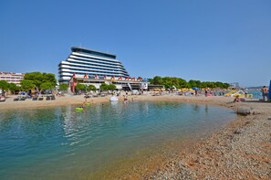 Una playa con un hotel moderno al fondo, cielos despejados y gente disfrutando del agua.