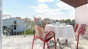 Un balcon avec une table et des chaises blanches, une vue sur les immeubles et un ciel dégagé.