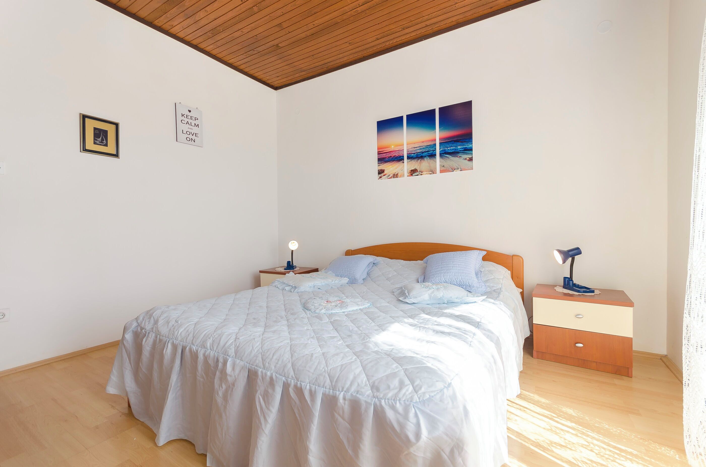 A bedroom with a bed, a nightstand, a lamp, and a wall with two framed pictures.